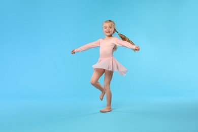 Photo of Cute little girl dancing on light blue background
