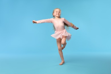 Photo of Cute little girl dancing on light blue background