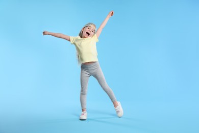 Photo of Cute little girl dancing on light blue background, space for text