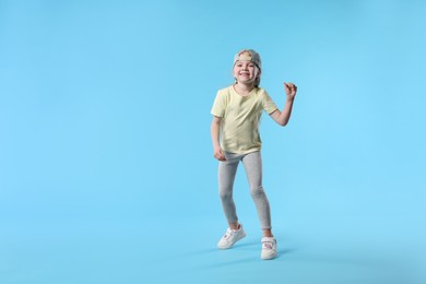 Photo of Cute little girl dancing on light blue background