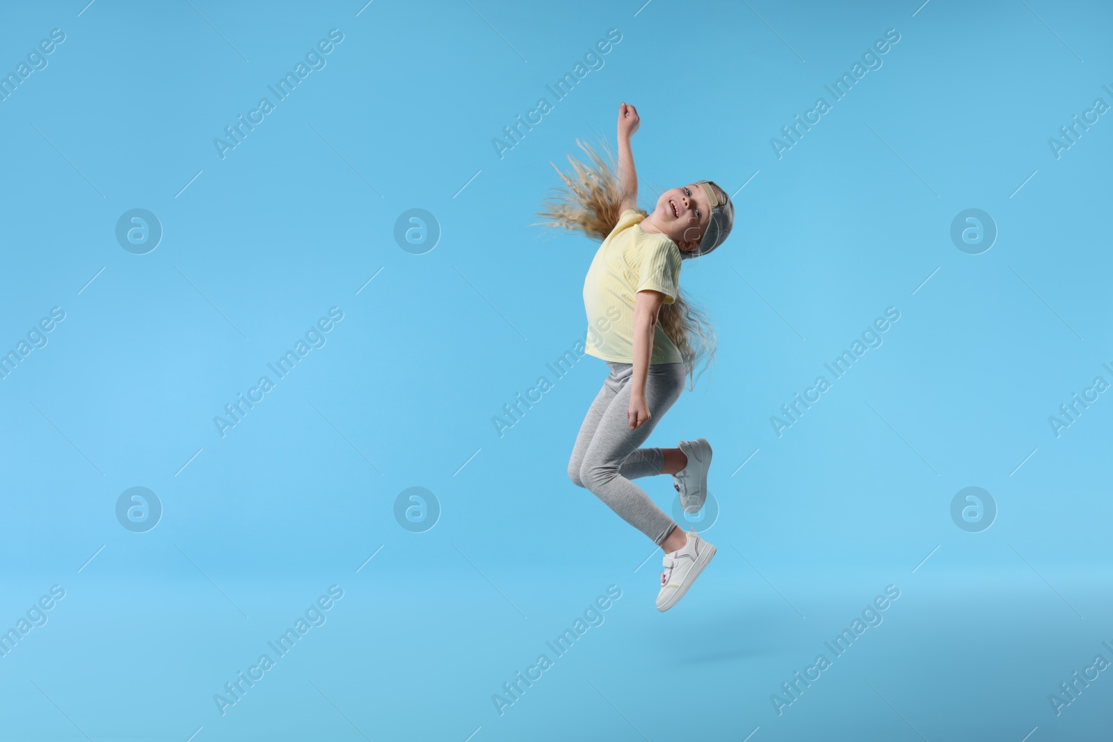 Cute little girl dancing on light blue background Photo of Cute little girl dancing on light blue background