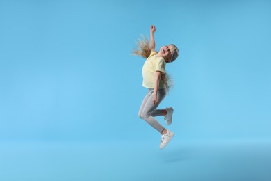 Photo of Cute little girl dancing on light blue background