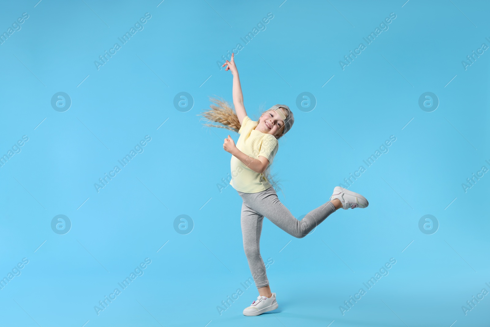 Cute little girl dancing on light blue background Photo of Cute little girl dancing on light blue background