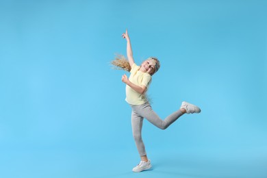 Photo of Cute little girl dancing on light blue background