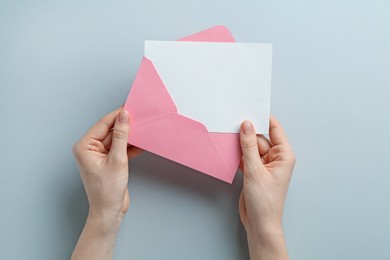 Photo of Woman holding envelope with blank invitation card on grey background, top view. Space for design