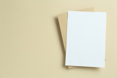 Photo of Blank invitation card and envelope on beige background, top view. Space for design