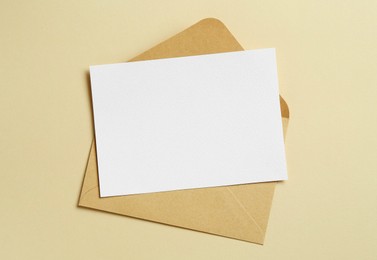 Photo of Blank invitation card and envelope on beige background, top view. Space for design