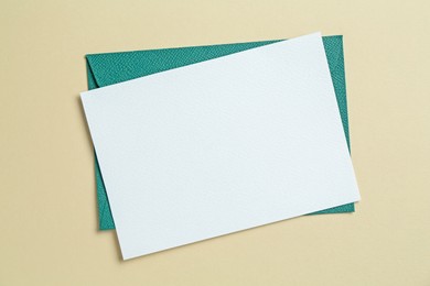 Photo of Blank invitation card and envelope on beige background, top view. Space for design
