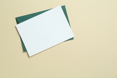 Photo of Blank invitation card and envelope on beige background, top view. Space for design