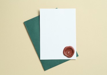 Photo of Blank invitation card with wax seal and envelope on beige background, top view. Space for design