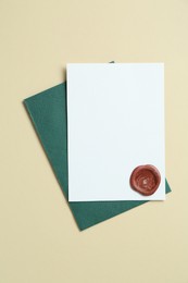 Photo of Blank invitation card with wax seal and envelope on beige background, top view. Space for design