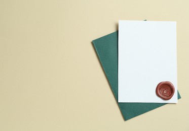 Photo of Blank invitation card with wax seal and envelope on beige background, top view. Space for design
