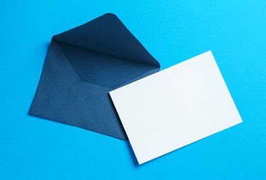 Photo of Blank invitation card and envelope on light blue background, top view. Space for design