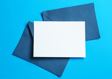 Photo of Blank invitation card and envelopes on light blue background, flat lay. Space for design