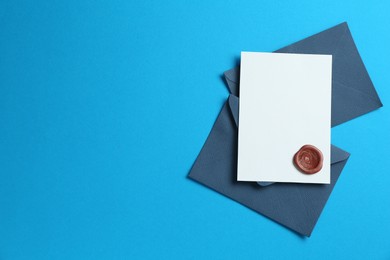 Photo of Blank invitation card with wax seal and envelopes on light blue background, flat lay. Space for design