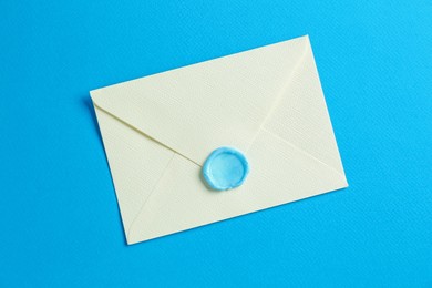 Photo of Beautiful invitation envelope with wax seal on light blue background, top view