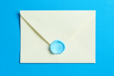 Photo of Beautiful invitation envelope with wax seal on light blue background, top view