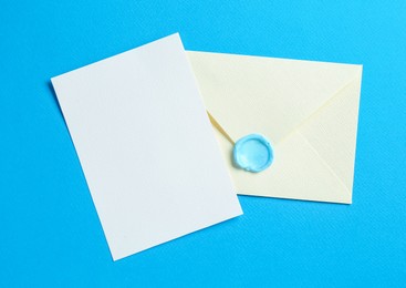 Photo of Blank invitation card and envelope on light blue background, top view. Space for design