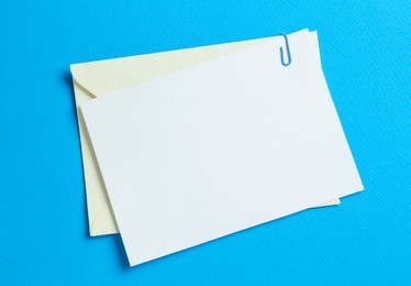 Photo of Blank invitation card and envelope on light blue background, top view. Space for design