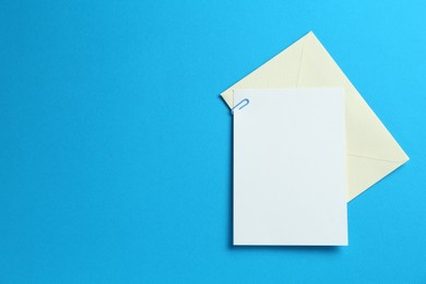 Photo of Blank invitation card and envelope on light blue background, top view. Space for design