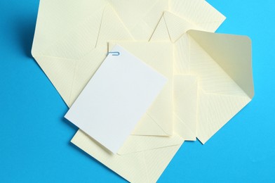 Photo of Blank invitation card and envelopes on light blue background, flat lay. Space for design