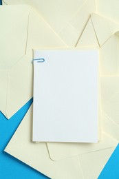 Photo of Blank invitation card and envelopes on light blue background, flat lay. Space for design