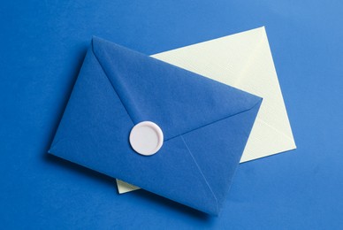Photo of Beautiful invitation envelope and card on blue background, top view