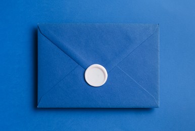 Photo of Beautiful invitation envelope with wax seal on blue background, top view