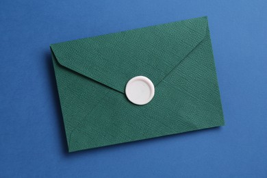 Photo of Beautiful invitation envelope with wax seal on blue background, top view