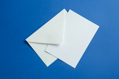 Photo of Blank invitation card and envelope on blue background, top view. Space for design