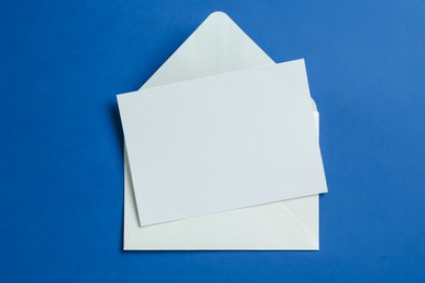Photo of Blank invitation card and envelope on blue background, top view. Space for design