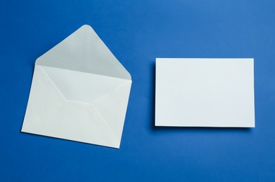 Photo of Blank invitation card and envelope on blue background, flat lay. Space for design