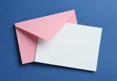 Photo of Blank invitation card and envelope on blue background, top view. Space for design