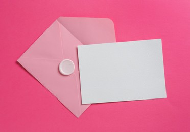 Photo of Blank invitation card and envelope on pink background, top view. Space for design