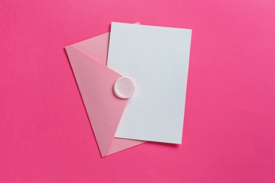 Photo of Blank invitation card and envelope on pink background, top view. Space for design