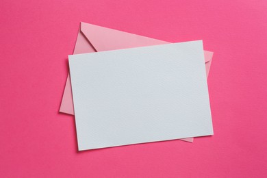 Photo of Blank invitation card and envelope on pink background, top view. Space for design