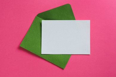 Photo of Blank invitation card and envelope on pink background, top view. Space for design