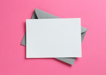 Photo of Blank invitation card and envelope on pink background, top view. Space for design