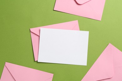 Photo of Blank invitation card and envelopes on green background, flat lay. Space for design