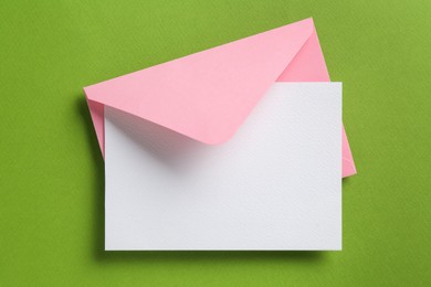 Photo of Blank invitation card and envelope on green background, top view. Space for design