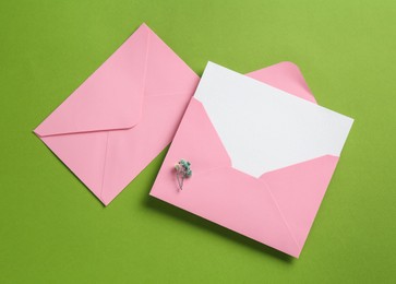 Photo of Blank invitation card and envelopes on green background, flat lay. Space for design