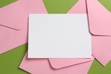Photo of Blank invitation card and envelopes on green background, flat lay. Space for design