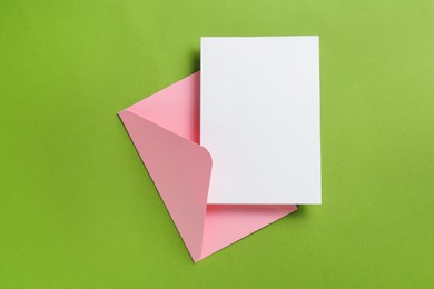 Photo of Blank invitation card and envelope on green background, top view. Space for design