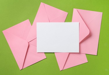 Photo of Blank invitation card and envelopes on green background, flat lay. Space for design