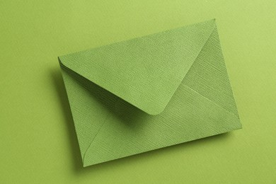 Photo of Beautiful invitation envelope on green background, top view
