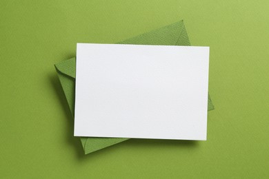 Photo of Blank invitation card and envelope on green background, top view. Space for design