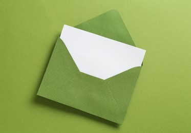 Photo of Blank invitation card and envelope on green background, top view