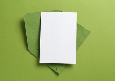Photo of Blank invitation card and envelope on green background, top view. Space for design