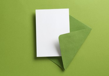 Photo of Blank invitation card and envelope on green background, top view. Space for design