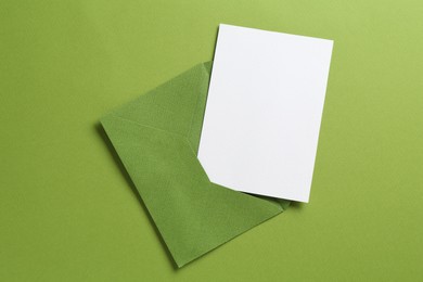 Photo of Blank invitation card and envelope on green background, top view. Space for design
